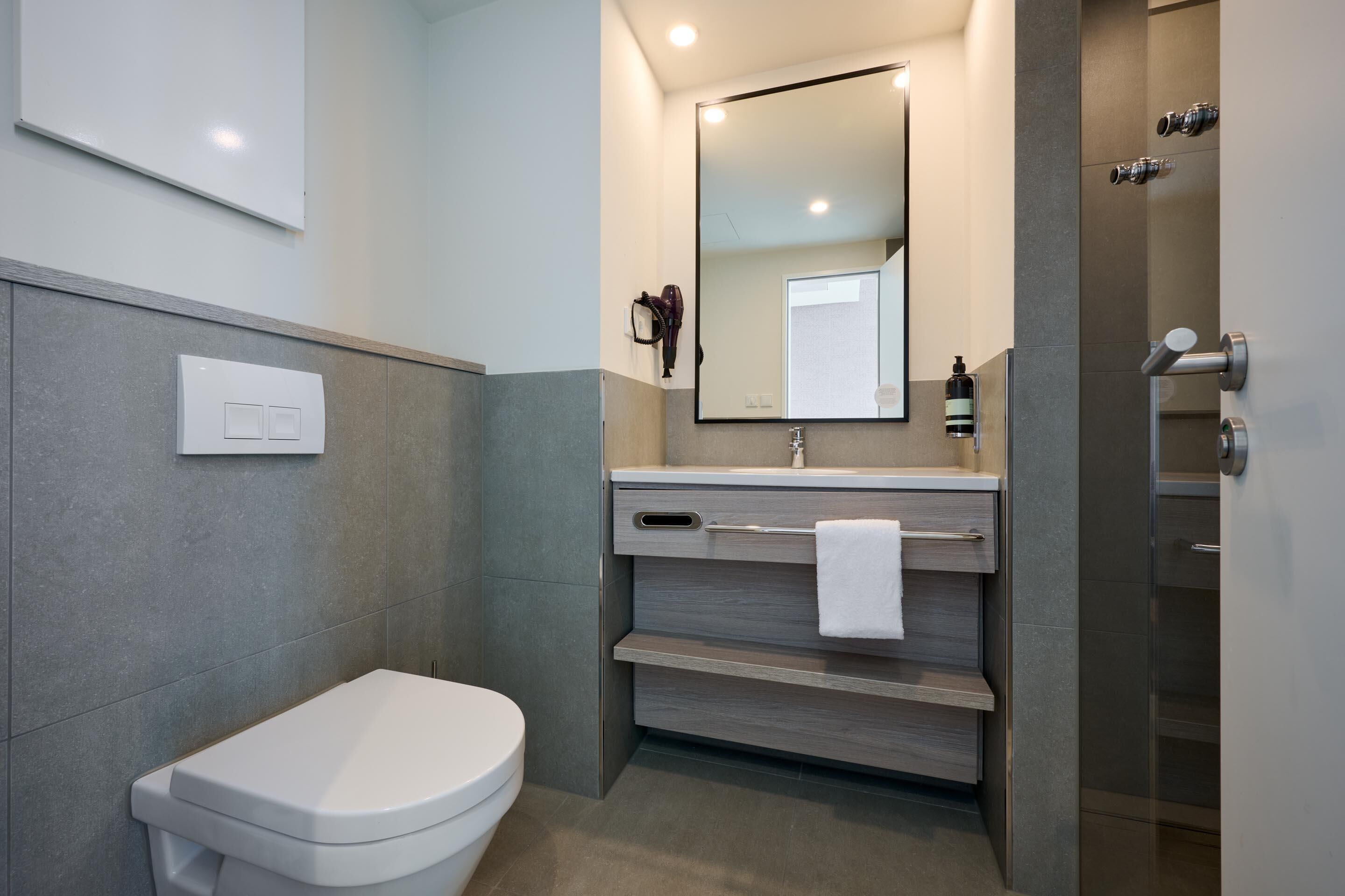 Un baño moderno con inodoro, lavamanos con espejo, toallero y zona de ducha.