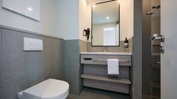 Un baño moderno con inodoro, lavamanos con espejo, toallero y zona de ducha.