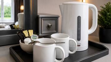 Een keukentafel met een koffiezetapparaat, twee witte mokken, een kom met koffiepads en een lepel.