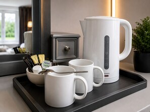 A kitchen counter with a coffee maker, two white mugs, a bowl with coffee pods, and a spoon.