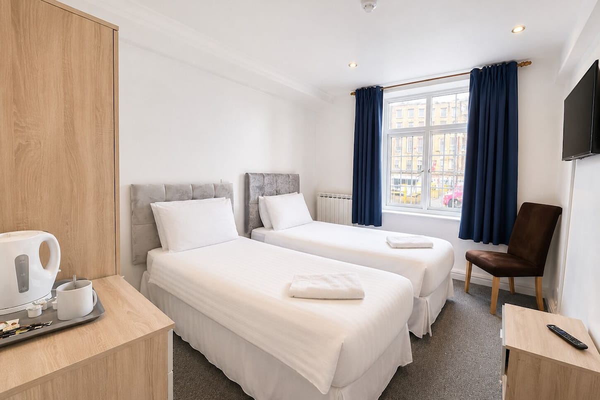 Ein Hotelzimmer mit zwei Betten, einem Holzschrank, einer Kaffeestation, einem Sessel und einem Fernseher.