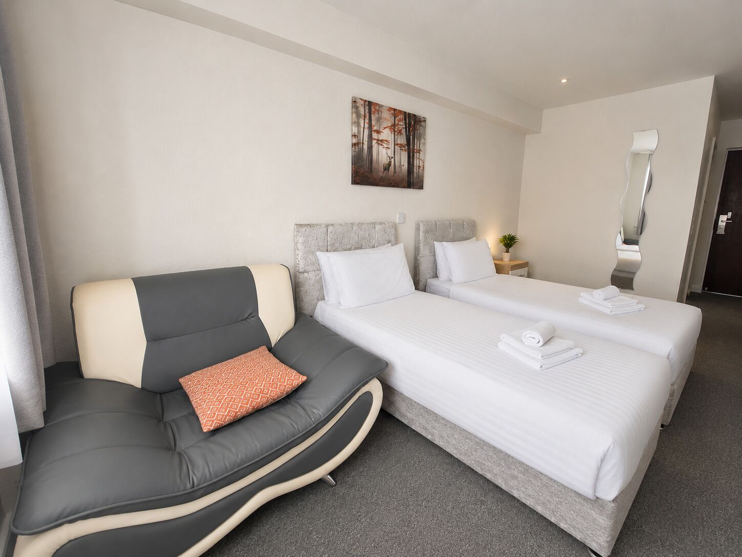 Una habitación de hotel con sofá, dos camas, un cuadro, una mesita de noche y un espejo.