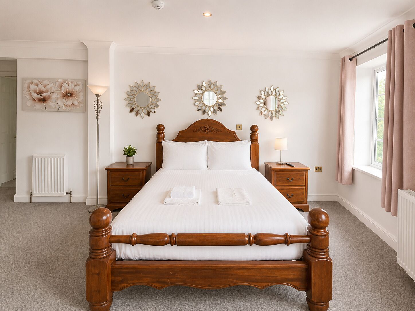 A neatly arranged bedroom with a wooden bed, bedside tables, a radiator, and decorative mirrors.