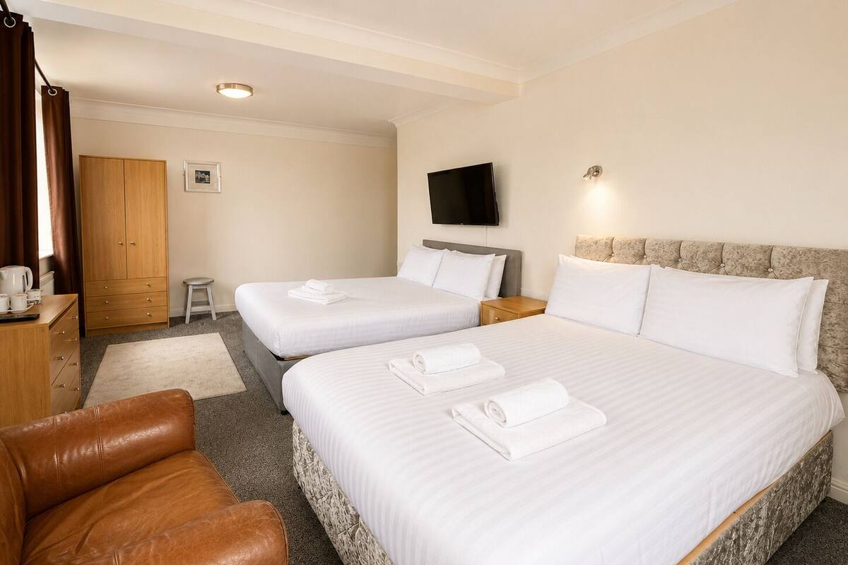 Ein Hotelzimmer mit zwei Betten, einem Fernseher, einem Kleiderschrank und einem Ledersessel.