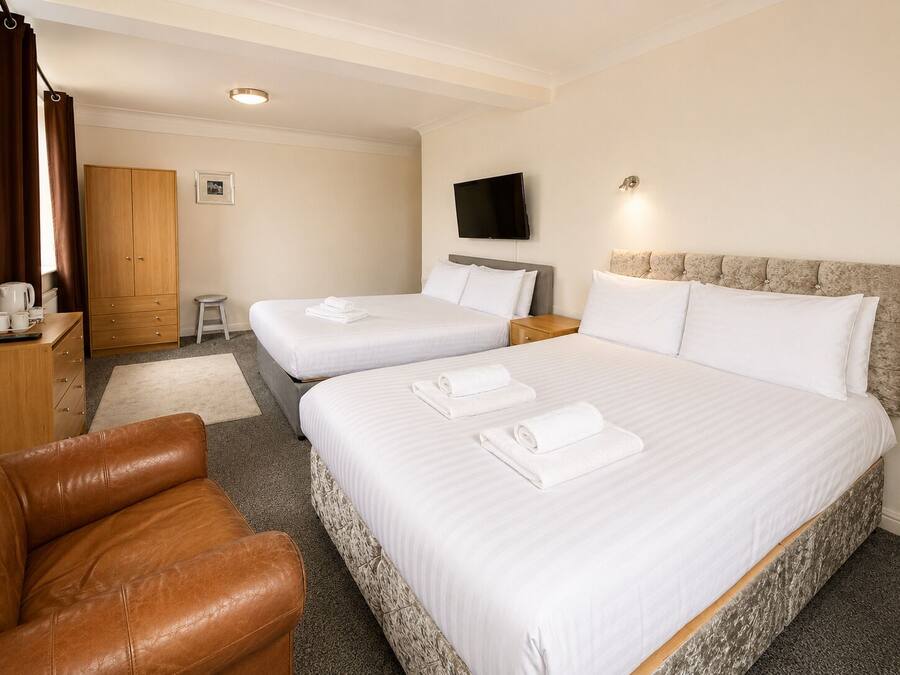A hotel room with two beds, a TV, a wardrobe, and a leather chair.