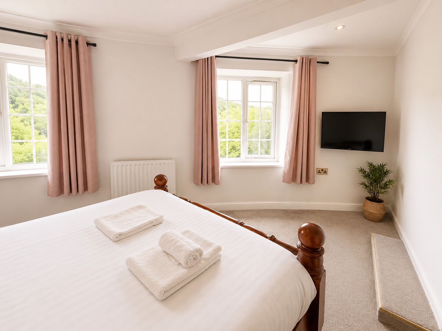 Een slaapkamer met een bed, twee handdoeken, een radiator, een televisie, een raam met gordijnen en een plant.