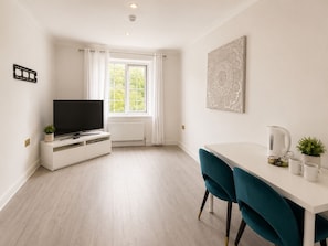 Ein modernes Zimmer mit Fernseher, weißen Möbeln, einem Fenster mit Vorhängen und einer Wanddekoration.