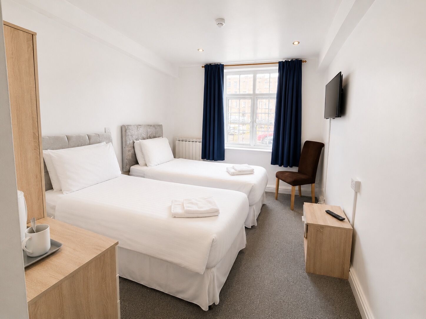A hotel room with two beds, a TV, a chair, and a small table with a remote control.