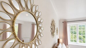 A bedroom with a large wall mirror, a bed with pillows, a window with curtains, and a radiator.