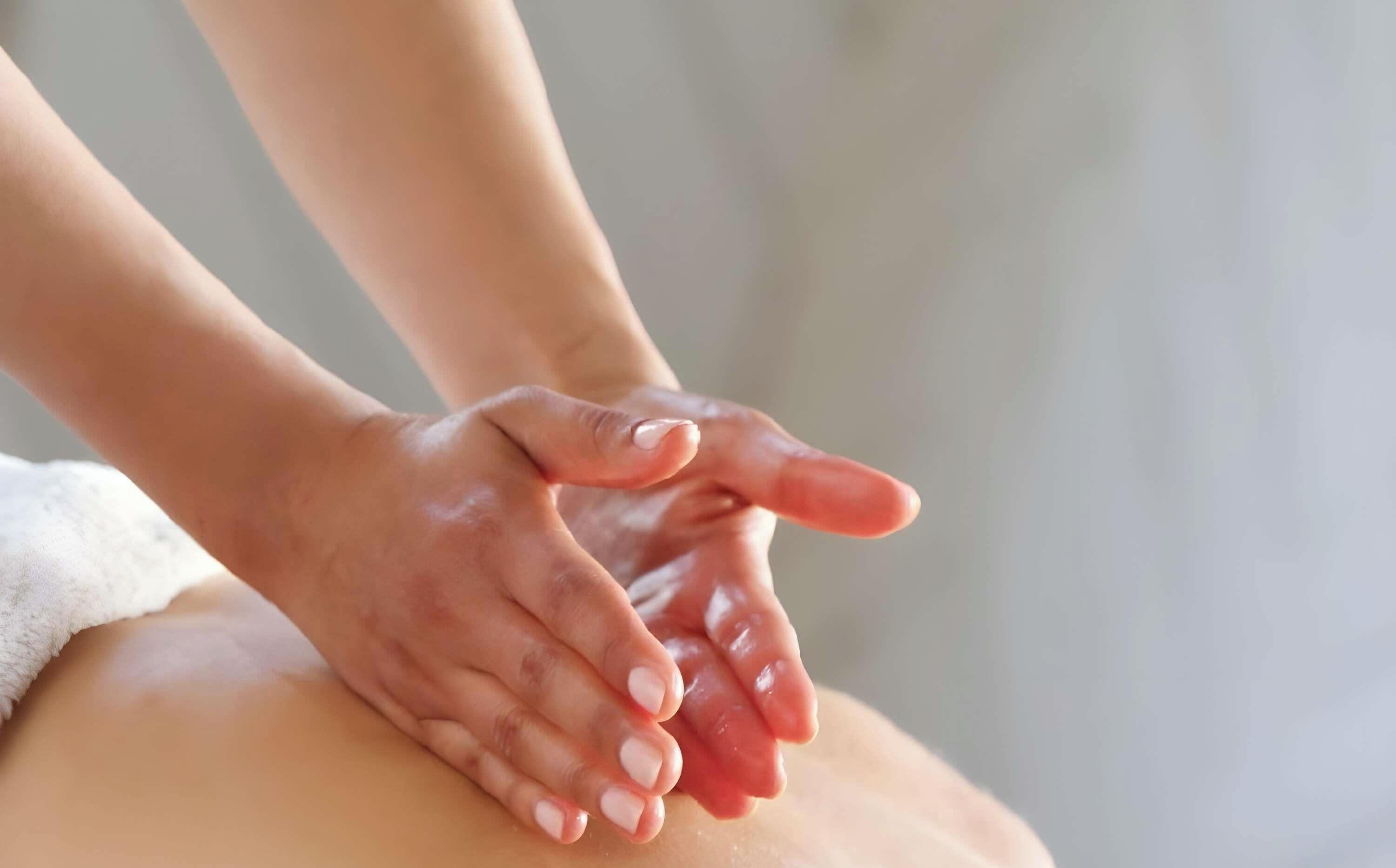Hands performing a massage on a person's back.