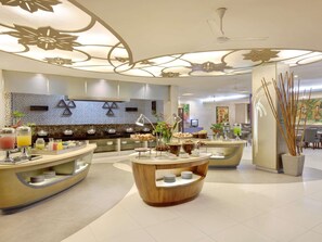 En moderne hotellobby med en central reception, buffetområde og et loft med dekorative mønstre.