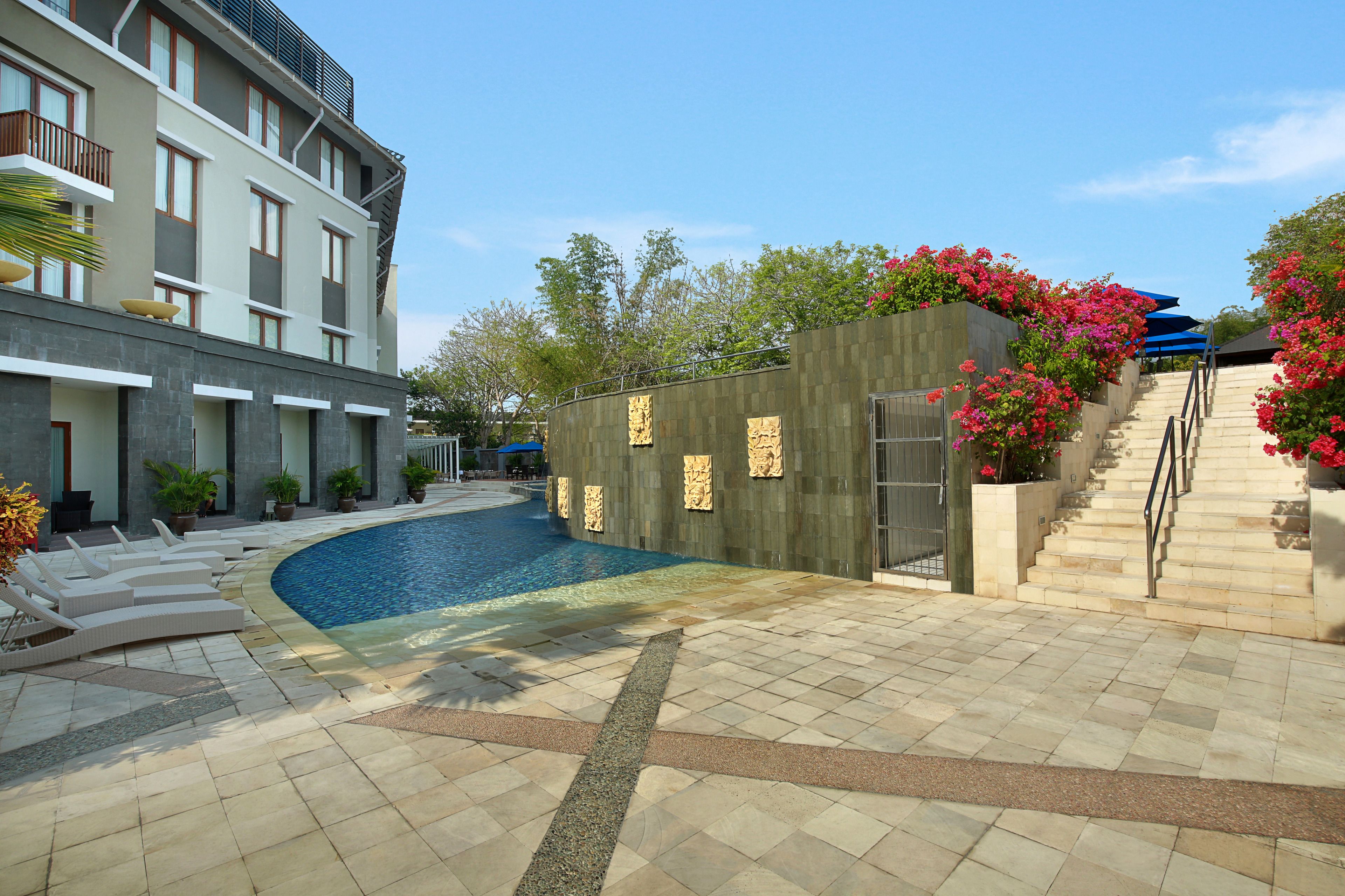 A modern hotel with a swimming pool, outdoor seating, and a staircase leading to a rooftop area.