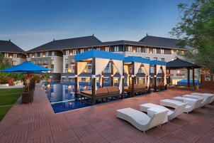 A hotel pool area with lounge chairs and umbrellas, a large pool, and a building with multiple balconies.