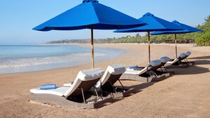 A beach with lounge chairs and blue umbrellas. - Mercure Bali Nusa Dua (Nusa Dua)