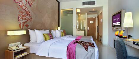 Habitación de hotel con una cama grande, un escritorio con computadora, televisor y baño visible a través de una puerta abierta.