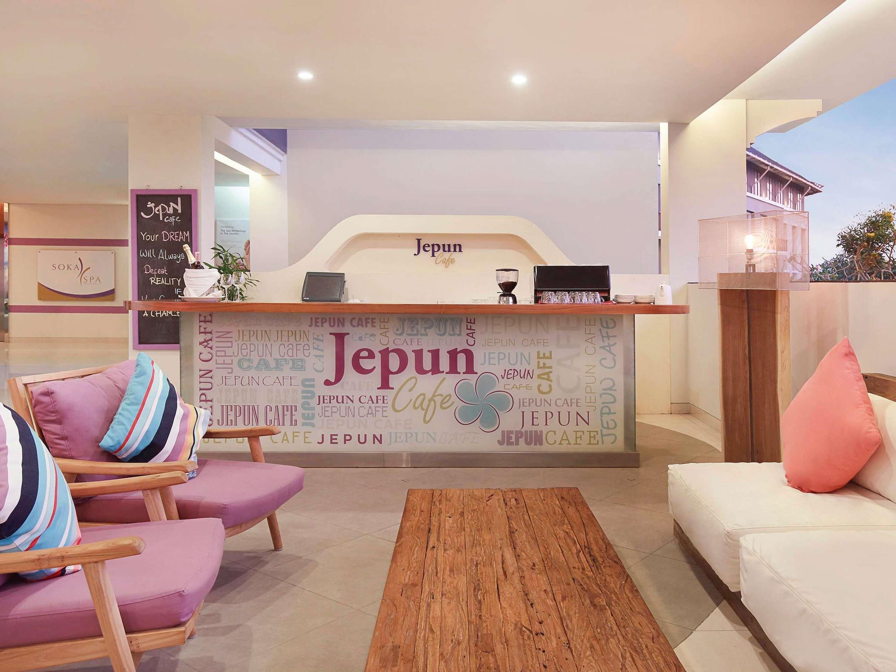 A reception area with a counter displaying 'Japun Cafe' and a sign for 'Soka Spa'. There are cushioned chairs and a wooden coffee table.