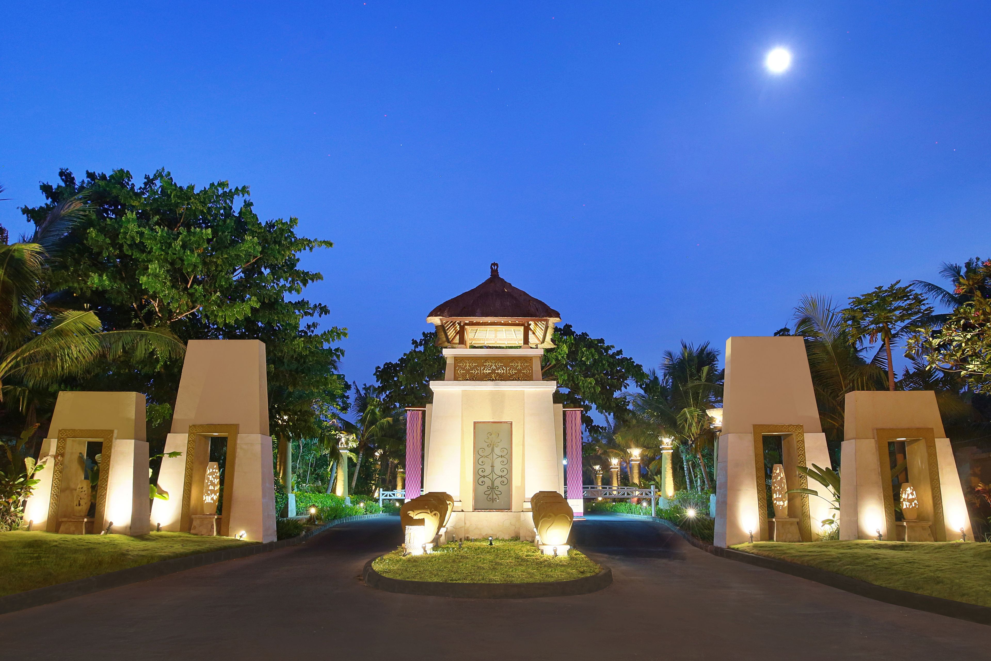 A well-lit entrance with a central pavilion, surrounded by symmetrical structures and lush greenery.