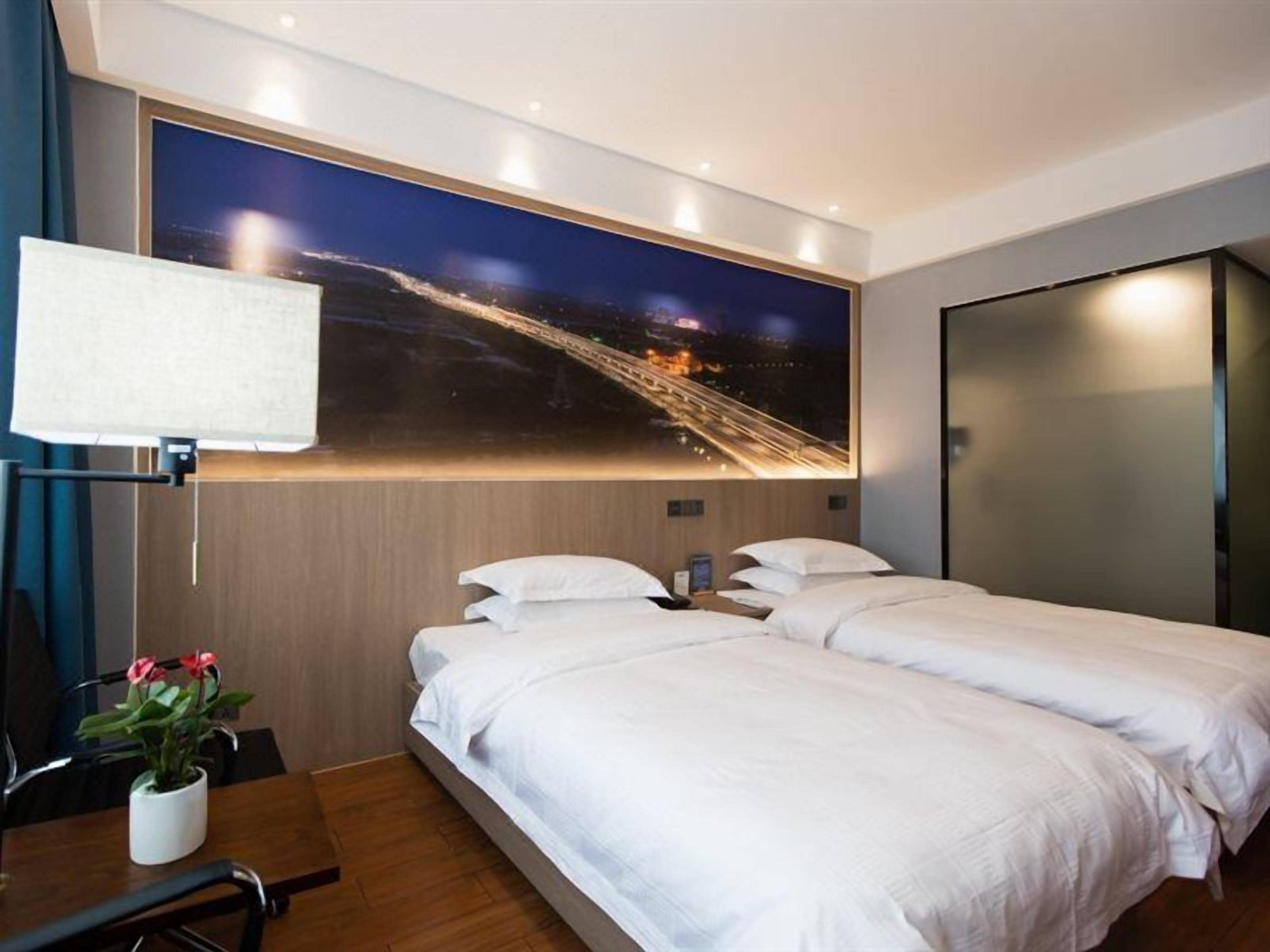 Una habitación de hotel con cama, escritorio, silla, lámpara y televisor instalado en la pared.
