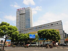 Un edificio de varios pisos con un letrero llamativo en la parte superior, rodeado de árboles y un cielo despejado.