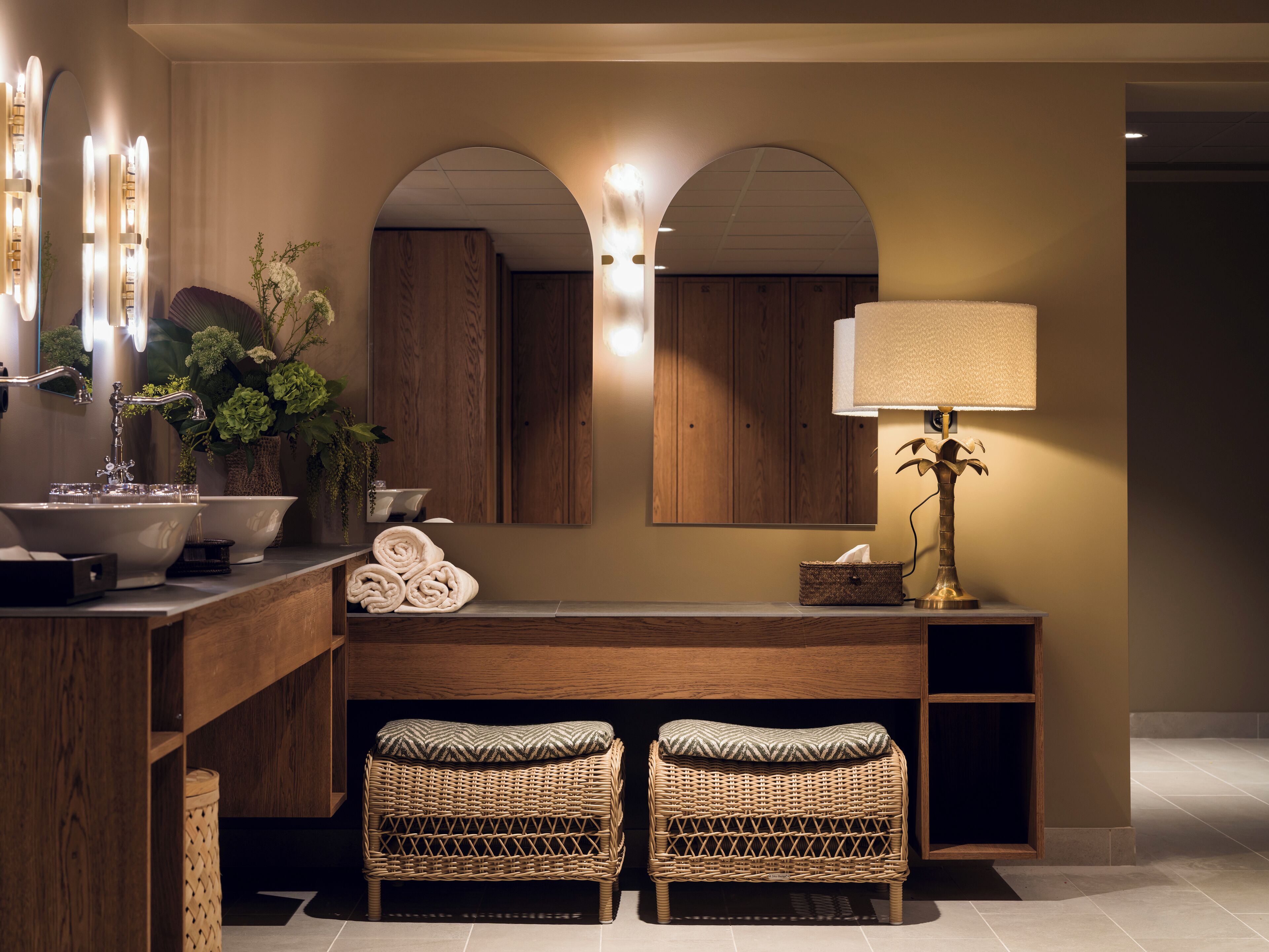 A bathroom with a large mirror, a sink, a towel rack, and two wicker stools.