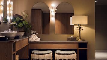 Une salle de bain avec un grand miroir, un lavabo, un porte-serviettes et deux tabourets en osier.