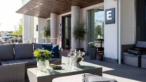 Un espace extérieur aménagé avec une table pour deux, un canapé et un vase décoratif contenant des bouteilles.