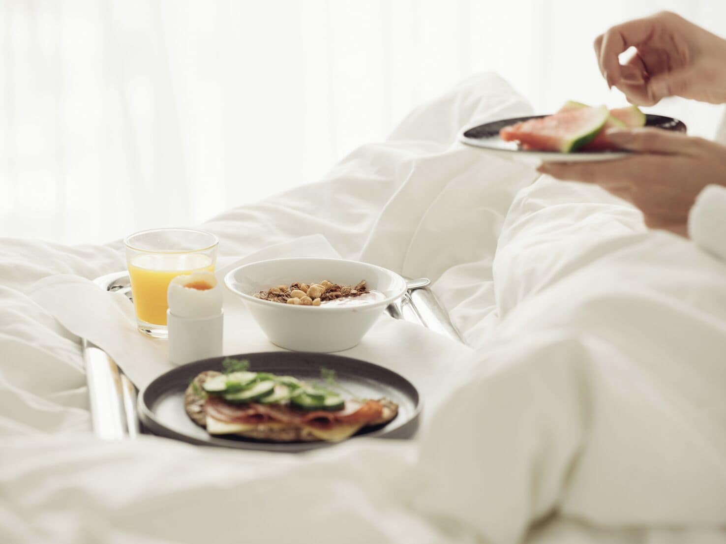 A bed with a breakfast tray containing cereal, a glass of orange juice, and a plate with a sandwich.