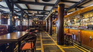A bar with wooden beams, a tiled floor, and a bar counter with bottles.
