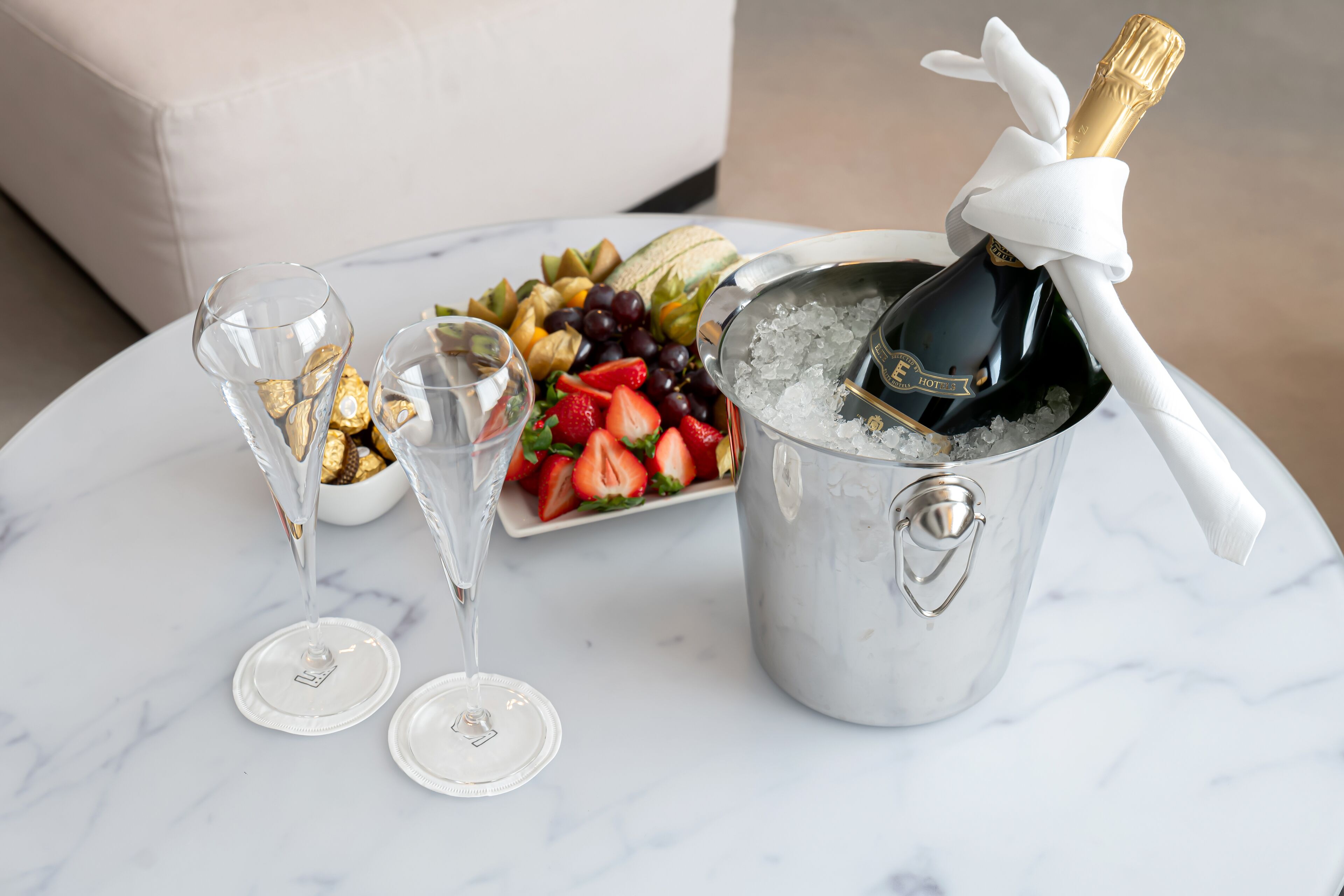 Une table avec une bouteille de champagne, deux verres à vin et une assiette de fruits.