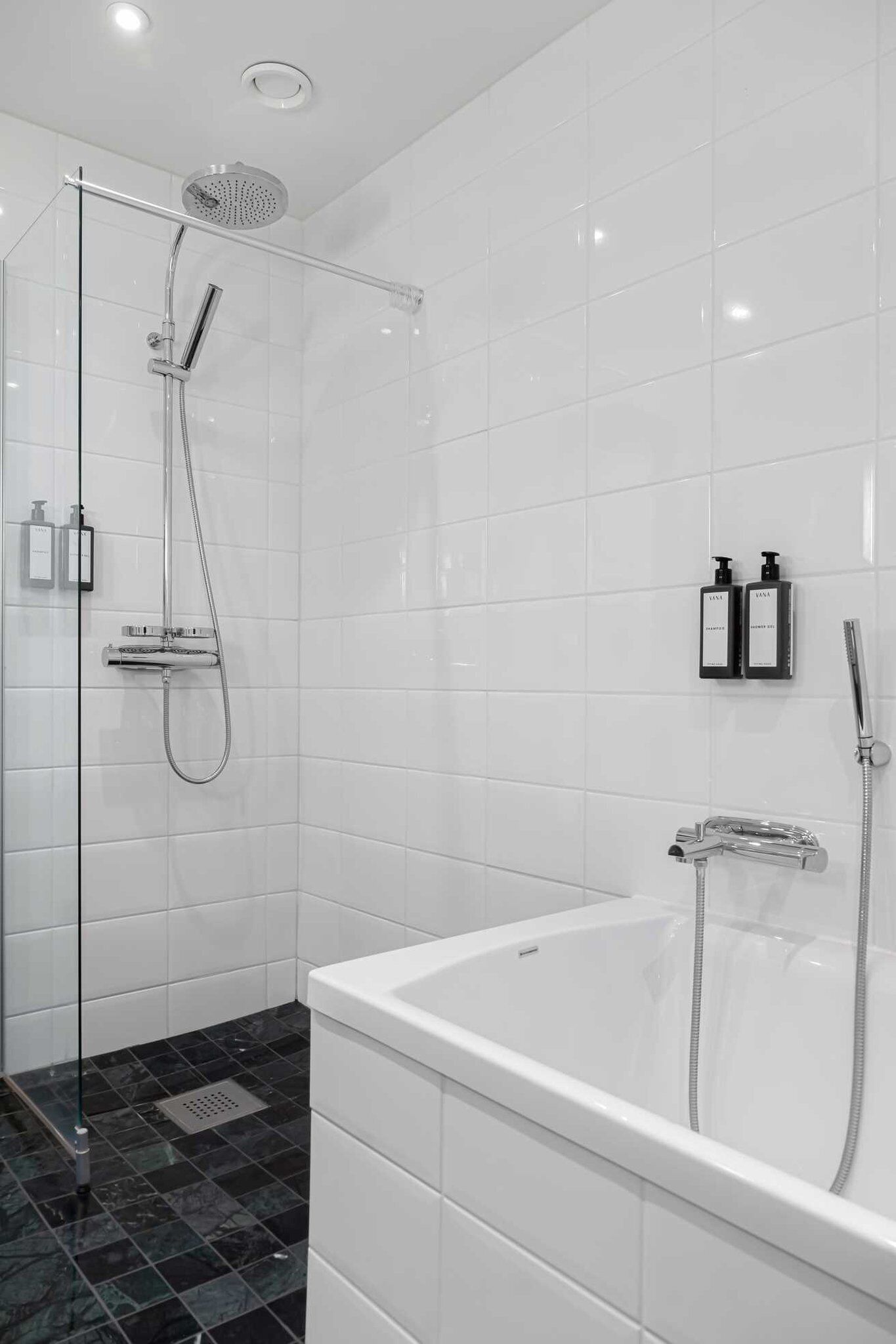Un baño moderno con cabina de ducha de vidrio, una bañera independiente y dos botellas de champú en la pared.