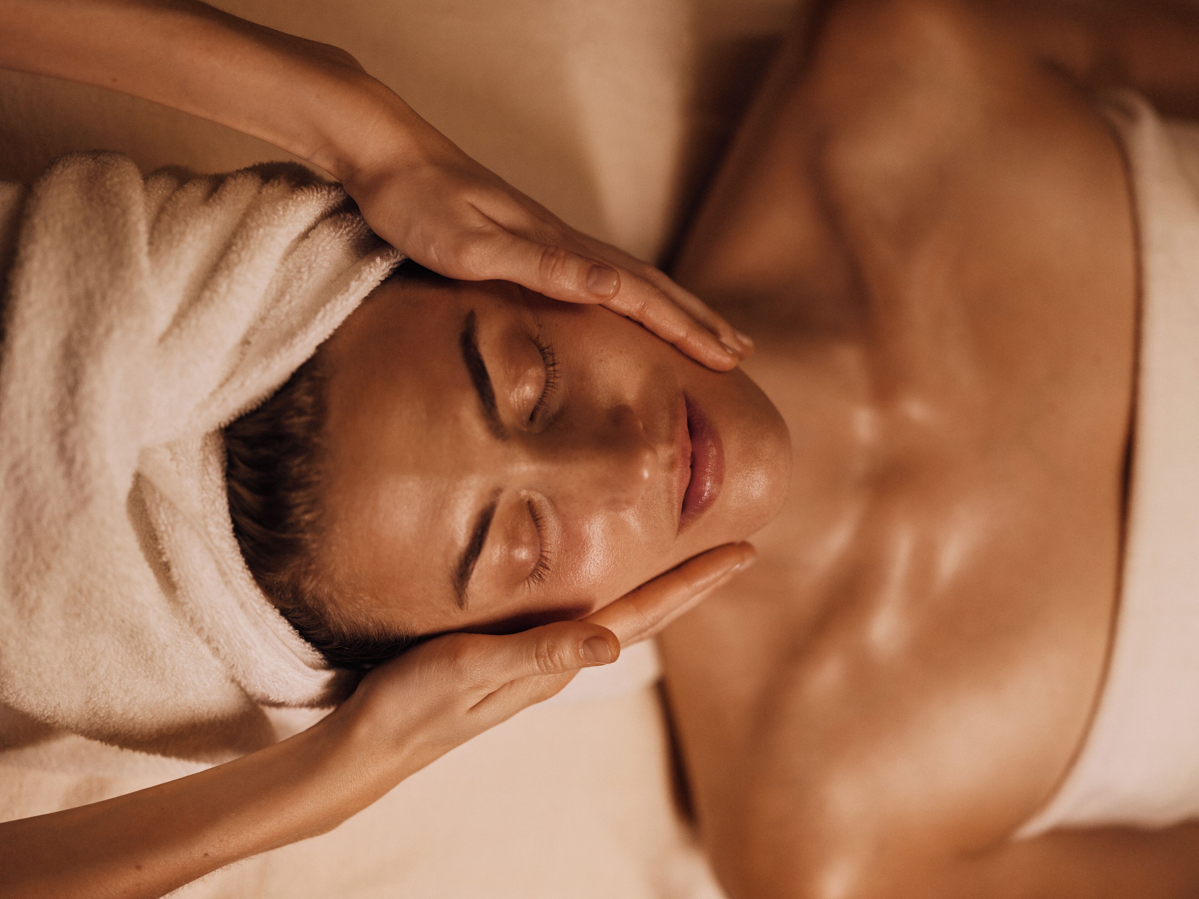 Una persona acostada con una toalla en la cabeza, evocando un ambiente de spa o relajación.