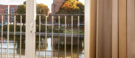 A view from a room with a window overlooking a historic building with two towers and a clock, a body of water, and a flag.