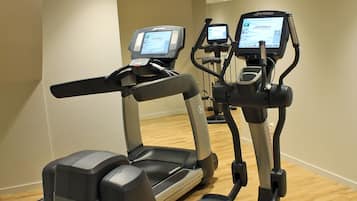 Ett gym med löpband och crosstrainers, trägolv och ett tak med infälld belysning.