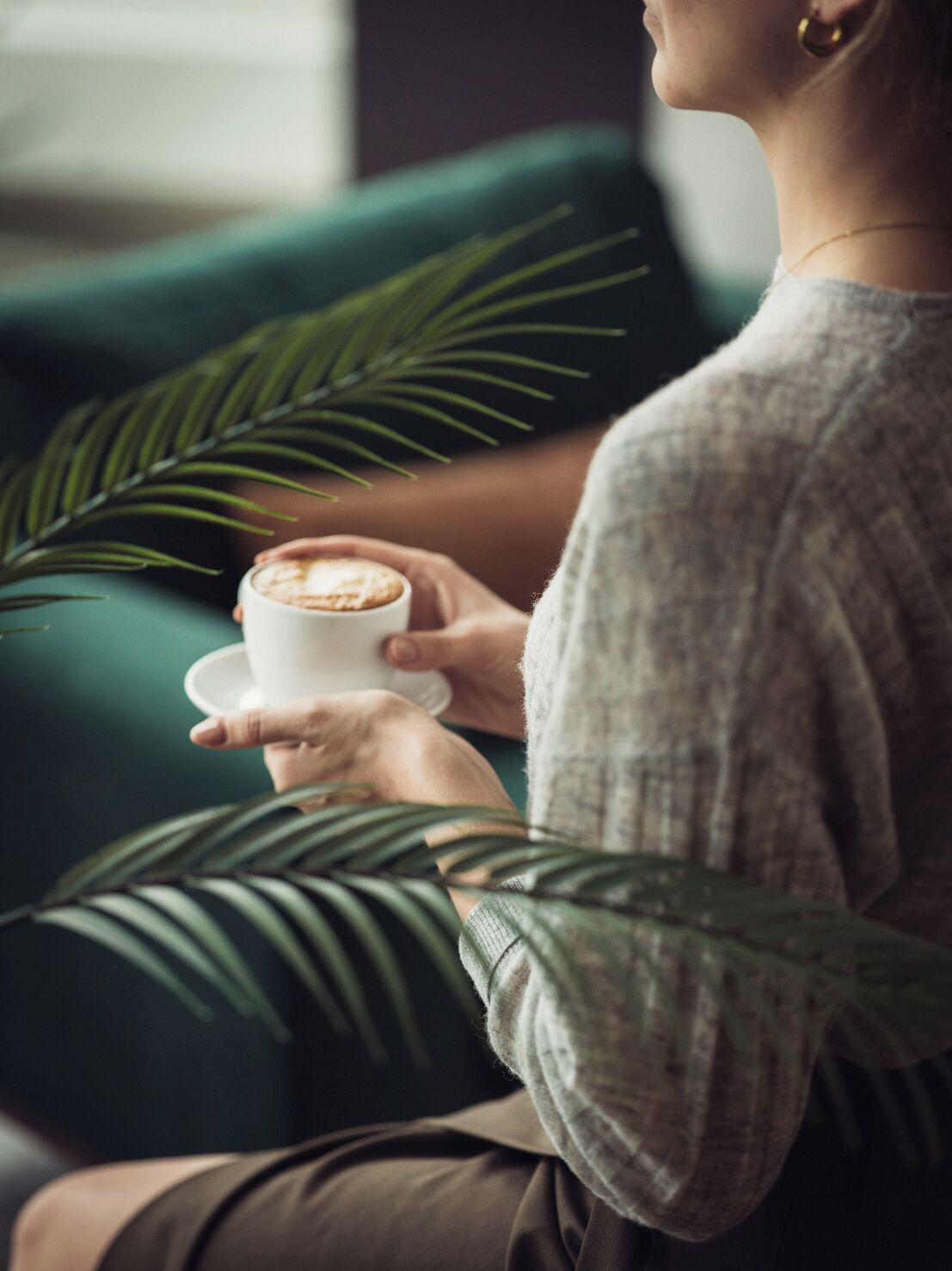 En person sitter på en grön soffa och håller i en kaffekopp.
