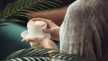En person sitter på en grön soffa och håller i en kaffekopp.