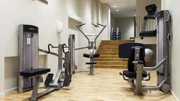 Un gimnasio con diversas máquinas de ejercicio, suelo de madera y una escalera al fondo.