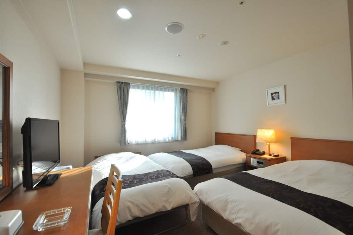 Ein Hotelzimmer mit zwei Betten, einem Schreibtisch mit Computer, einer Lampe und einem Fenster mit Vorhängen.