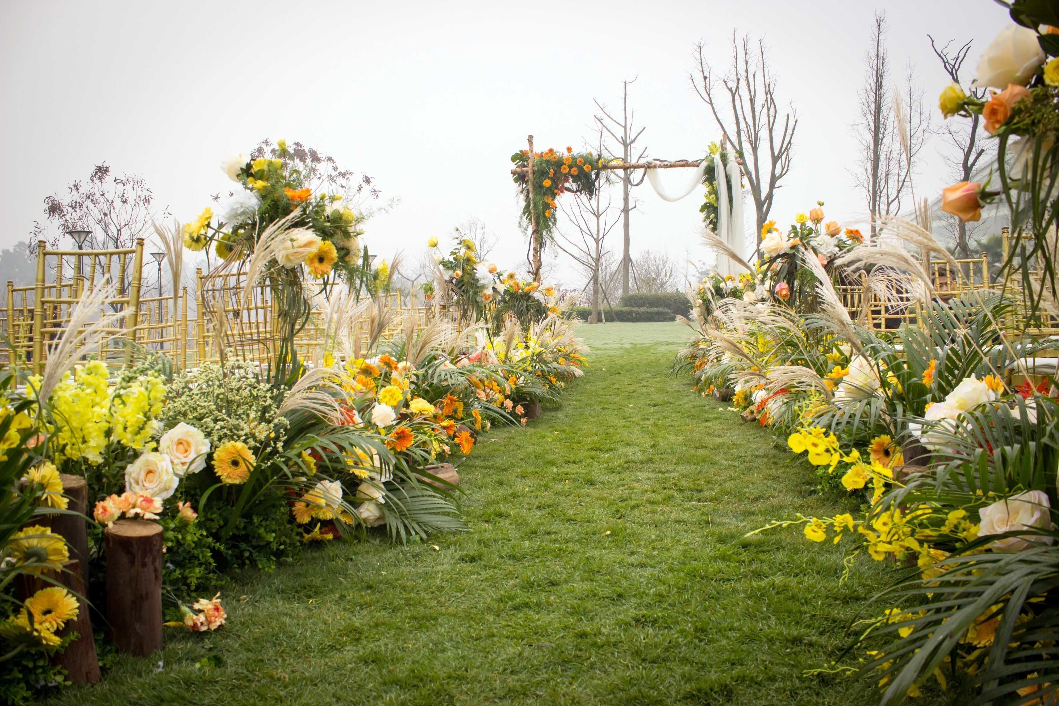 A pathway lined with floral arrangements and a rustic archway.