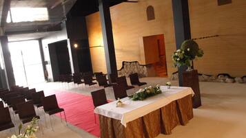 Un amplio salón con filas de sillas, una mesa central con mantel blanco y una alfombra roja.