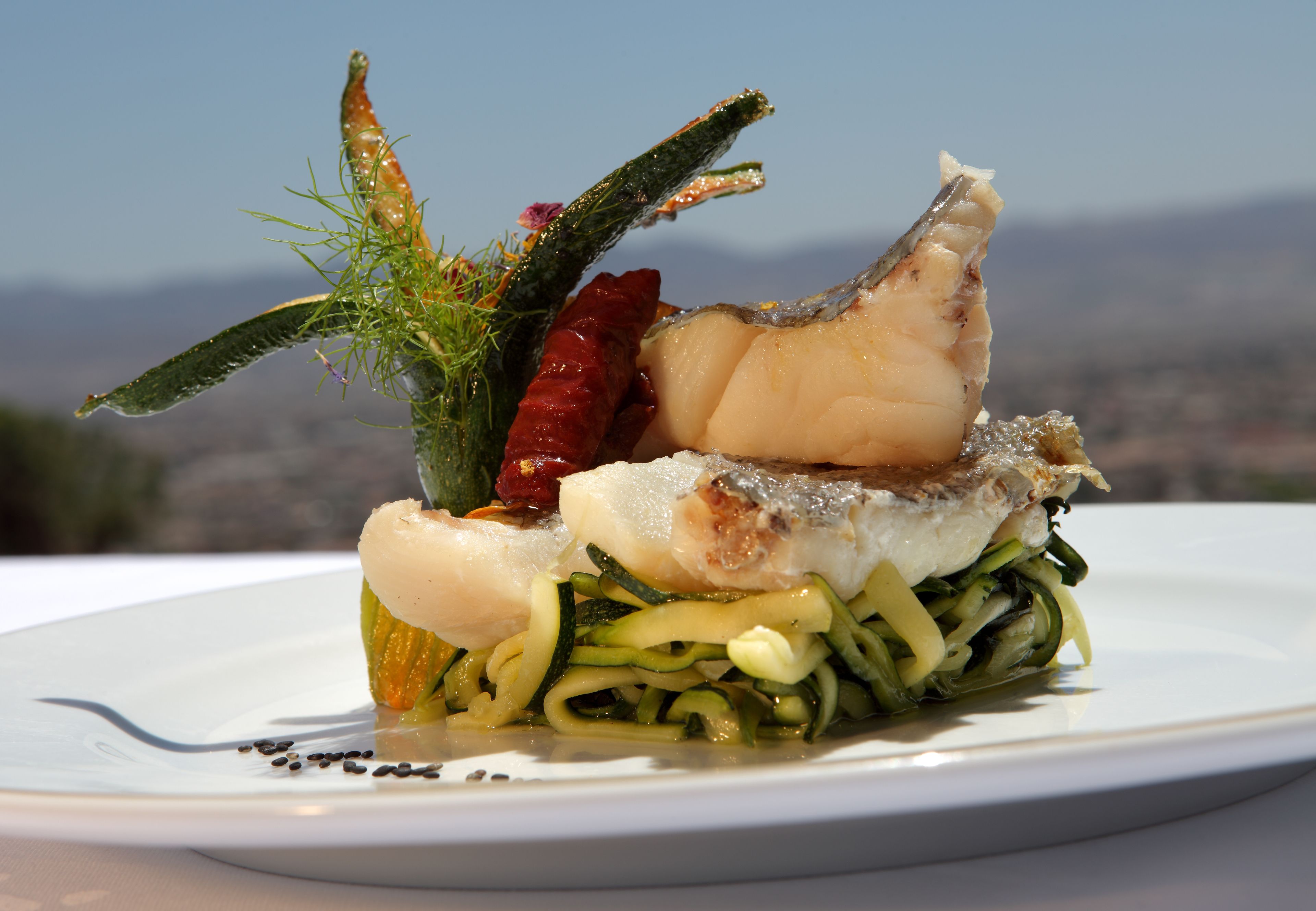 Plat de marisc amb peix, carbassa i guarnicions sobre un plat blanc.