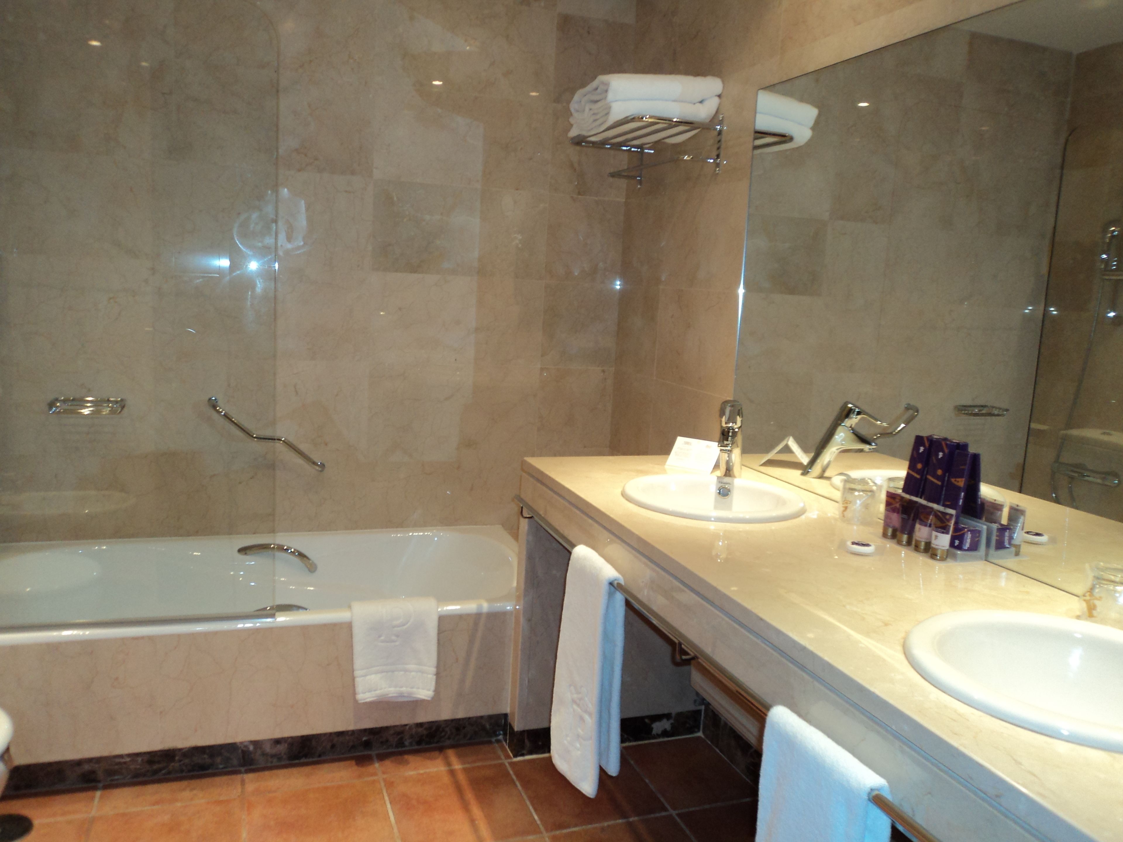 A bathroom with a bathtub, two sinks, a mirror, and a towel rack.