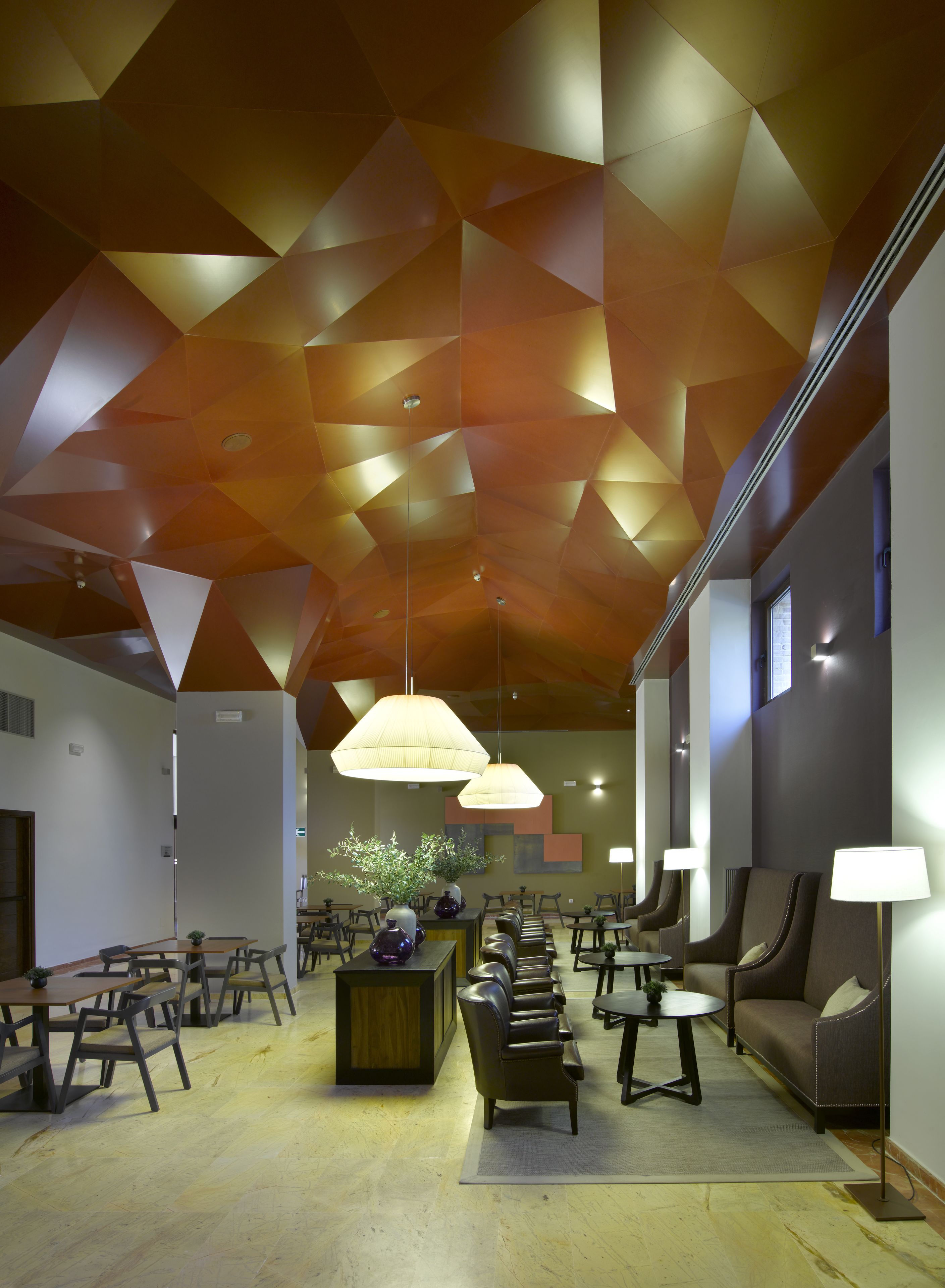 En moderne lobby med geometrisk loftsdesign, siddepladser og stemningsbelysning.