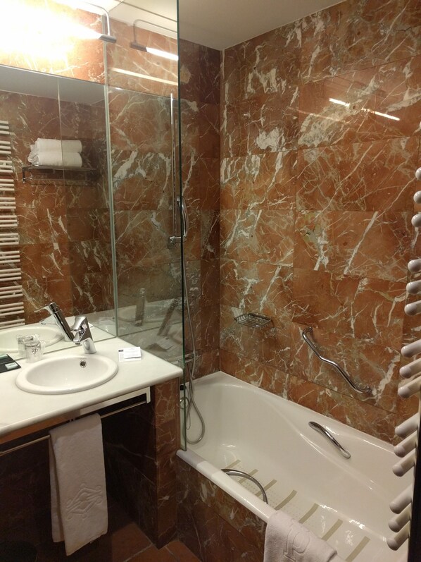 A bathroom with a marble wall, a sink, a mirror, a glass shower enclosure, and a bathtub.