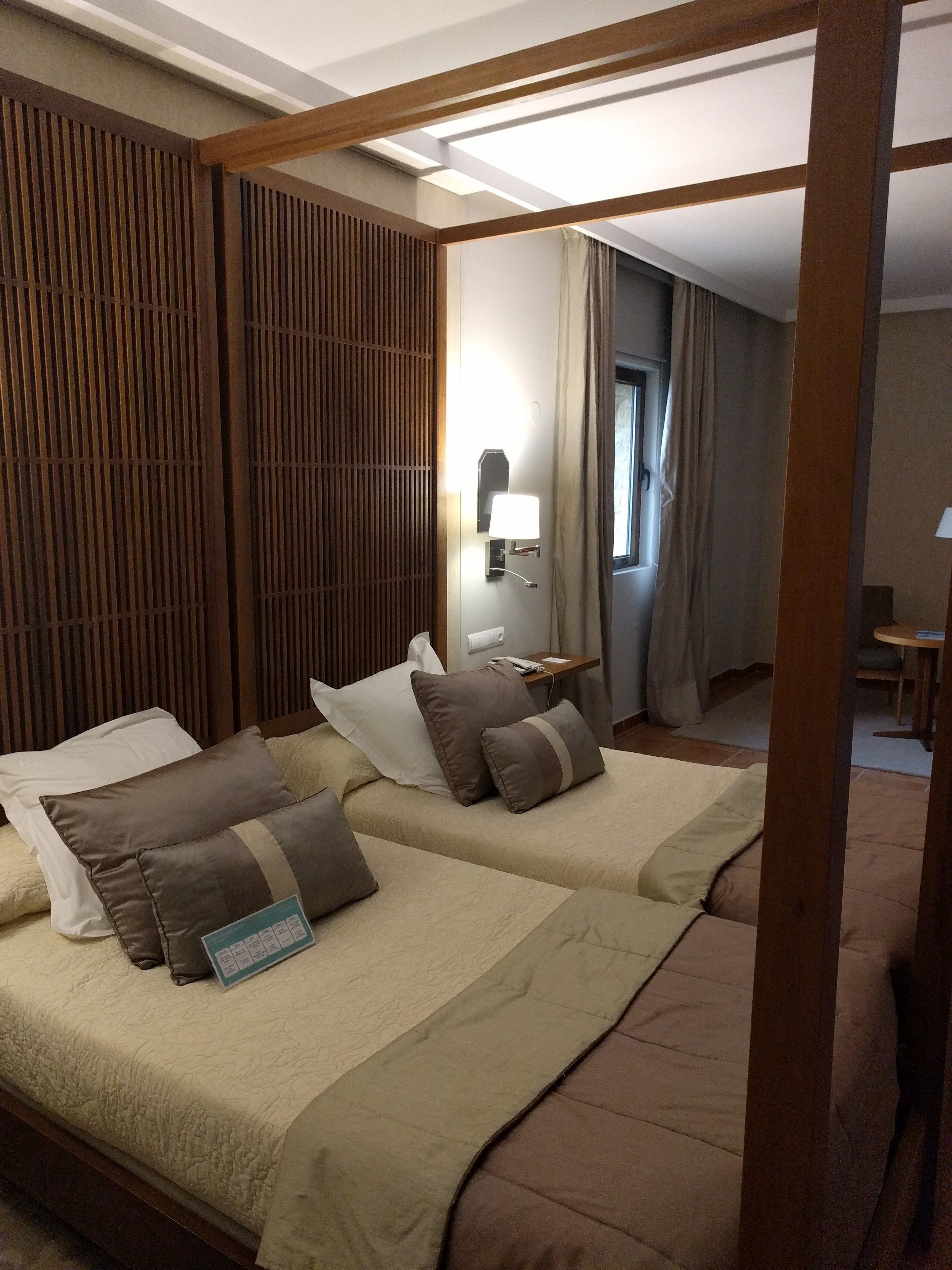 Ein Hotelzimmer mit Bett, Nachttisch, Lampe und einem Fenster mit Vorhängen.
