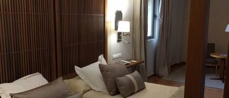 Una habitación de hotel con una cama, una mesita de noche, una lámpara y una ventana con cortinas.