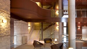 A spacious lobby with a modern design, featuring a curved ceiling, a staircase, and seating areas with tables and chairs. - Parador de Lorca (Lorca)