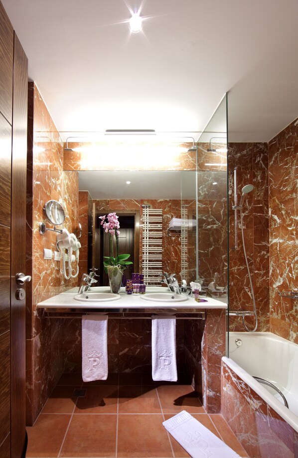 A modern bathroom with a marble vanity, dual sinks, a large mirror, a glass-enclosed shower, and a white bathtub.