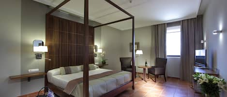 Ein Hotelzimmer mit einem Himmelbett, einem Nachttisch, einem Sessel, einem Fernseher und einem kleinen Tisch mit Lampe.