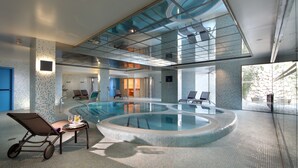 An indoor swimming pool with a glass ceiling, lounge chairs, and a sunbed. - Parador de Lorca (Lorca)