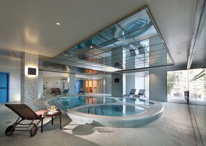 Relax by the pool surrounded by lounge chairs in a spacious area with a glass ceiling.